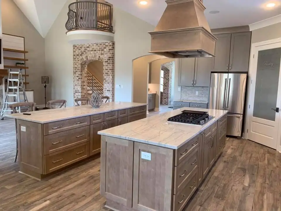 Two taupe shaker cabinet islands with white veined stone tops and a wood range hood, kitchen cabinets in Memphis by HCS Kitchen and Bath