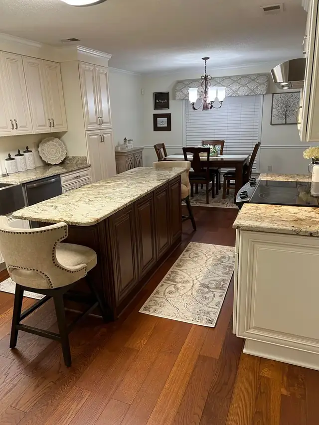 Kitchen island with dark stained raised panel cabinets and a gold and cream granite countertop, cream perimeter cabinets behind